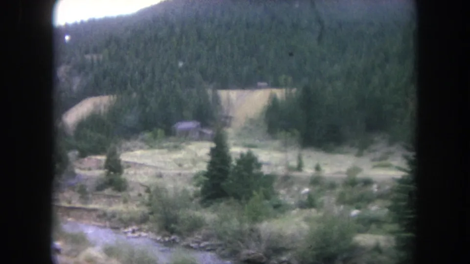Soft 8mm Colorado mountain-drive frame with creek, meadowland, evergreens, and a forested slope in Winter Park.
