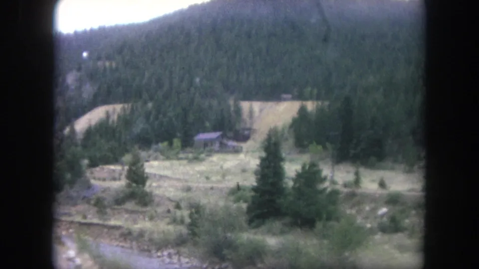 1962 Winter Park 8mm view across a creek and evergreens toward a small meadow and dense mountain forest.