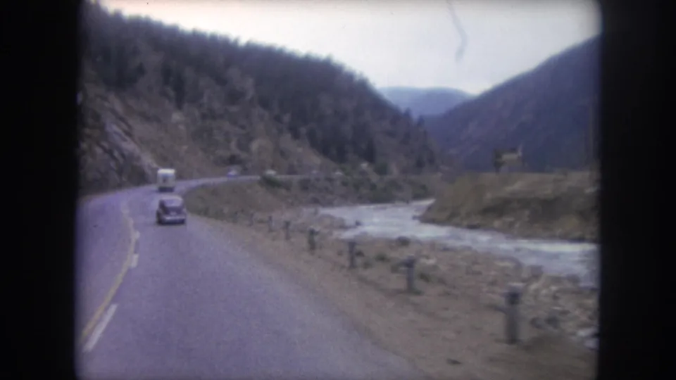End frame of the Winter Park highway drive shows a dark sedan ahead, river to the right, forested slopes, and a yellow roadside sign.