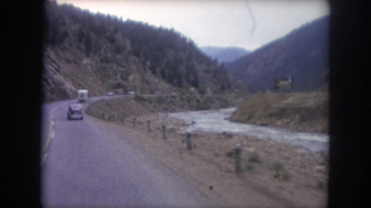 Car and white van on a curving mountain road beside a rocky river.