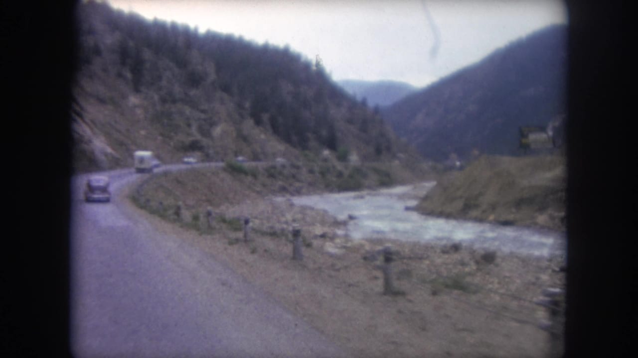 A moving-vehicle view of a Winter Park mountain road, with cars ahead and a pale river running through the valley.