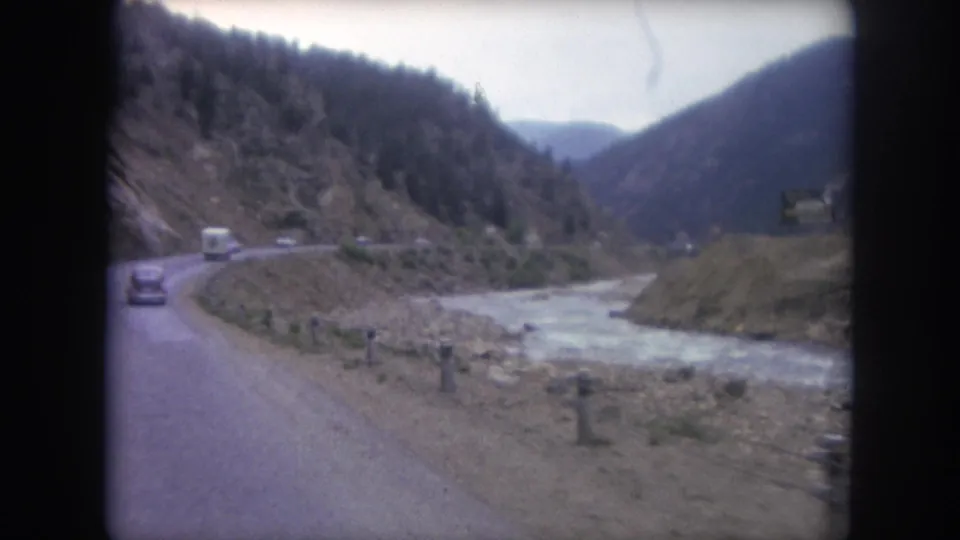 A moving-vehicle view of a Winter Park mountain road, with cars ahead and a pale river running through the valley.