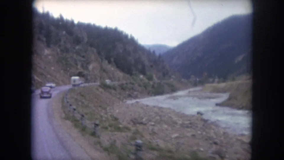 Final frame of the Winter Park road sequence, showing cars on the curve and the river continuing through the mountain valley.