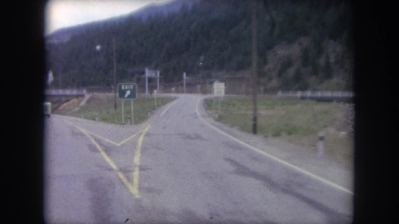 Two-lane mountain road approaching a junction with a green exit sign.