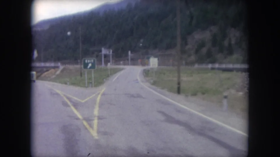 1962 Winter Park, Colorado road footage showing a two-lane mountain junction, painted lane markings, and a green exit sign near forested slopes.