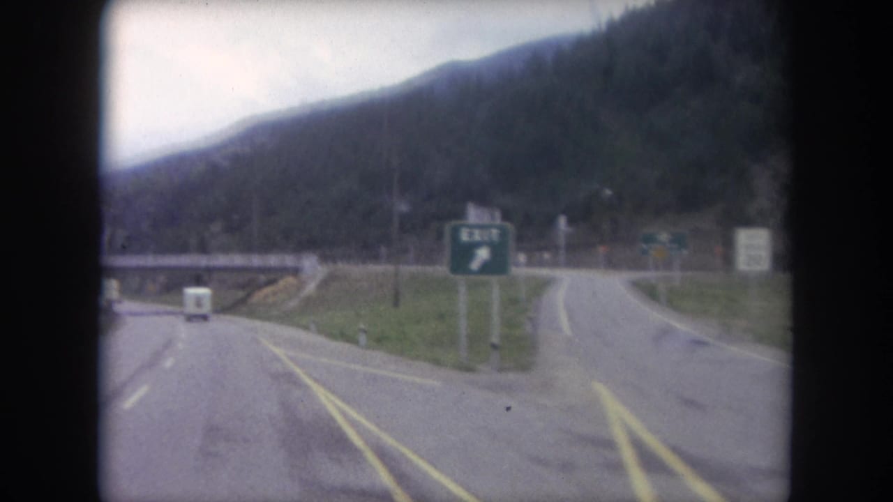 A 1962 Winter Park, Colorado road scene with a green exit sign, small white vehicle, bridge structure, and curving mountain road.