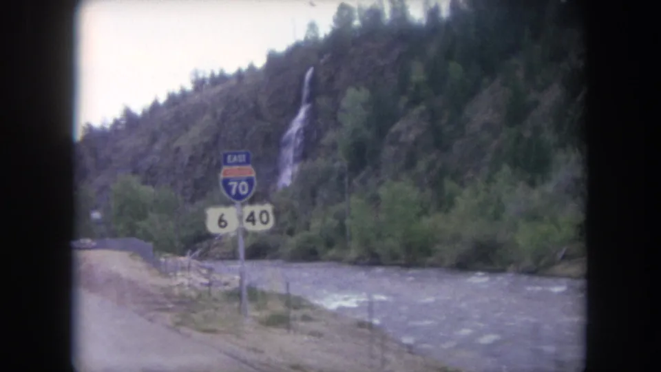 1962 Colorado highway scene showing U.S. Route 6 and 40 shields, an Interstate 70 East sign, the river, and a waterfall on the mountainside.