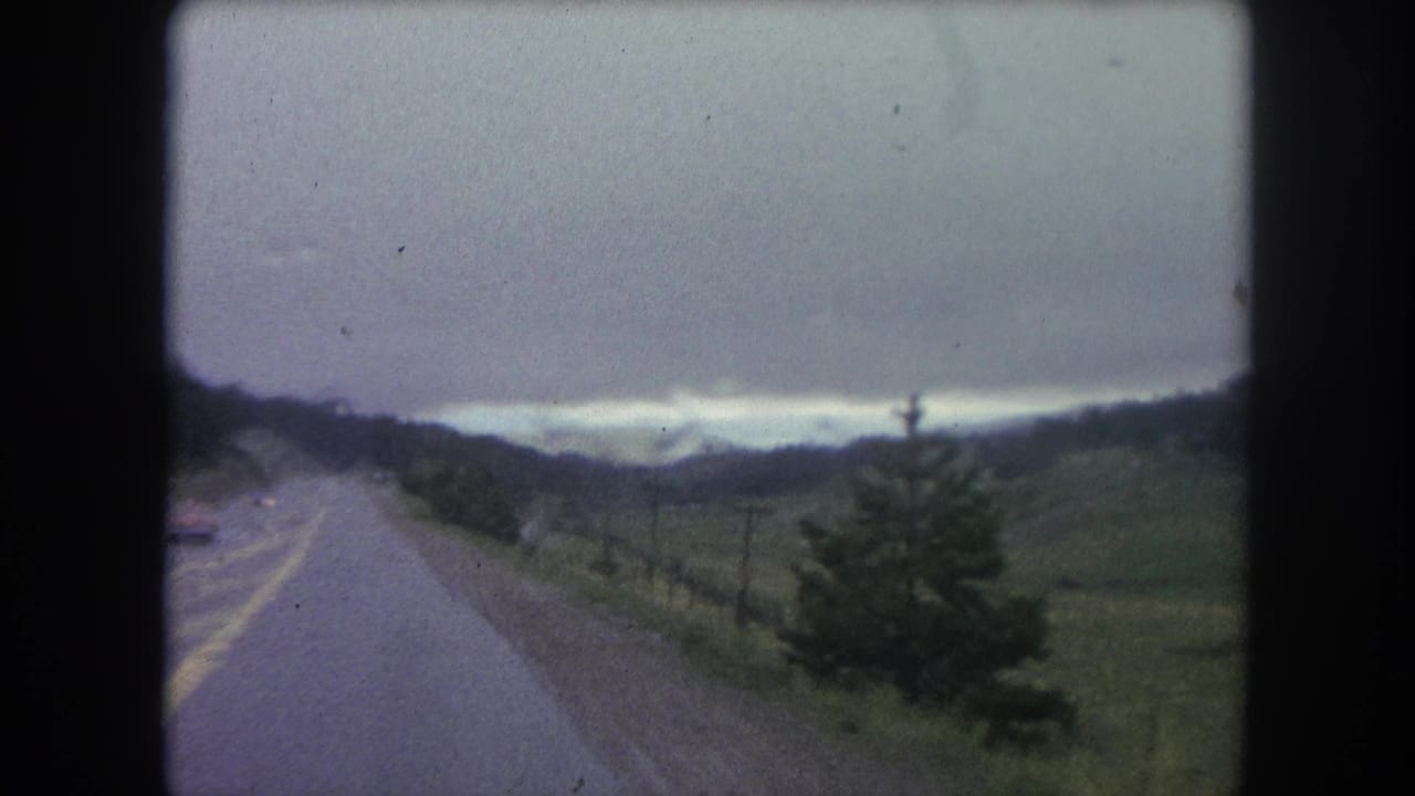 1962 8mm view from a moving car on a rural road near Winter Park, Colorado, with hills, trees, and distant mountains.