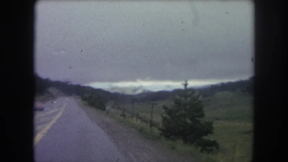 1962 8mm view from a moving car on a rural road near Winter Park, Colorado, with hills, trees, and distant mountains.