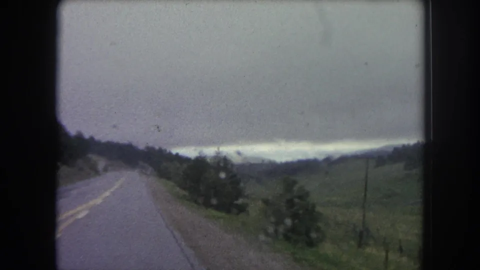 Vintage 8mm frame of a road trip through rural Winter Park, with roadside vegetation and distant mountain slopes.