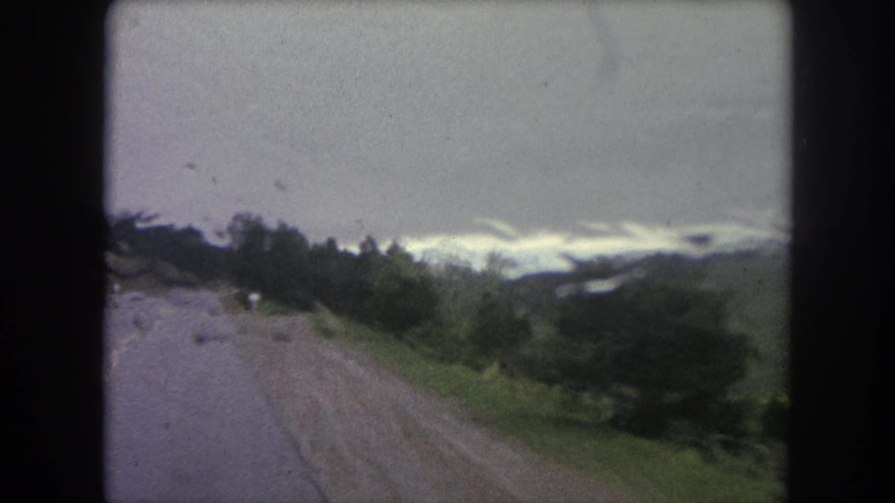 A moving 8mm view near Winter Park shows the wet road curving past trees and green terrain under gray clouds.