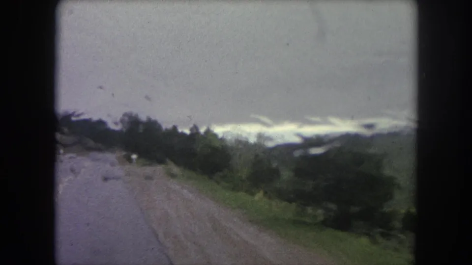 A moving 8mm view near Winter Park shows the wet road curving past trees and green terrain under gray clouds.
