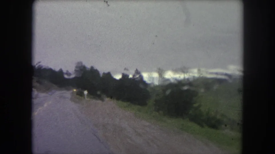The 1962 Colorado travel view remains rain-darkened, with a wet road, trees, and soft 8mm motion blur.