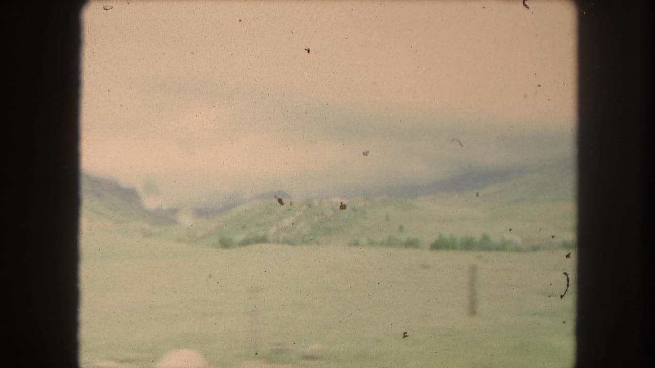 Soft view of green hills and distant mountains through a dark vehicle window frame.