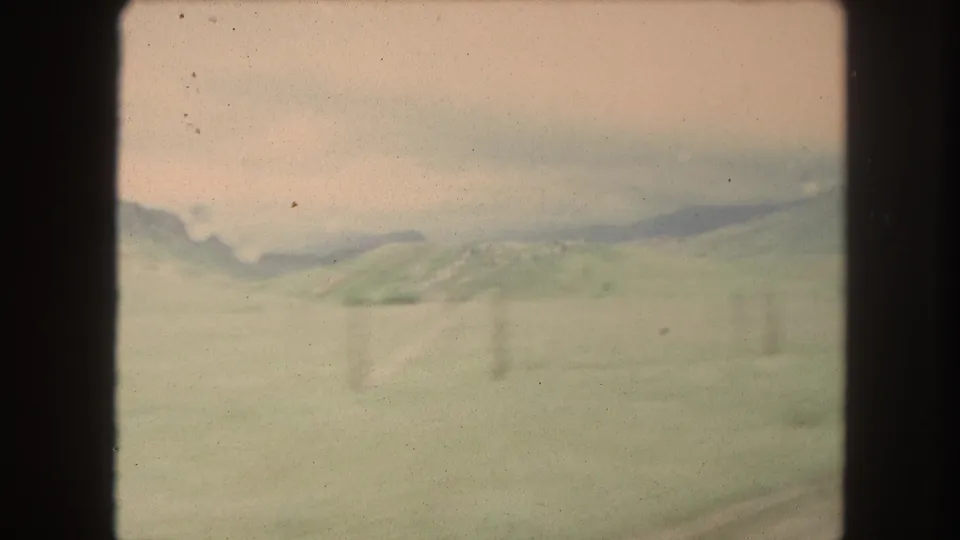 1962 Winter Park, Colorado passing landscape with pale green hills, low mountains, overcast sky, and blurred fence posts.
