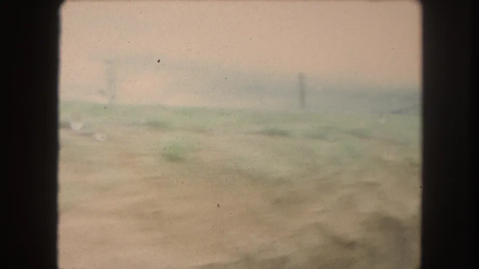 1962 Winter Park, Colorado home-movie frame showing blurred roadside ground, fence posts, low hills, and a cloudy sky from a moving vehicle.