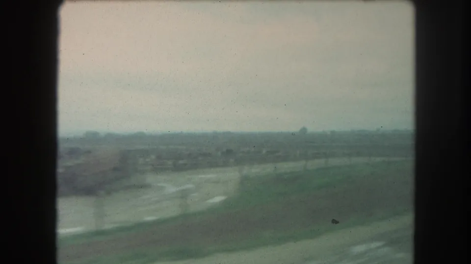 Soft 1962 Winter Park, Colorado home-movie frame looking across open ground and a pale road or track toward a low, hazy horizon.