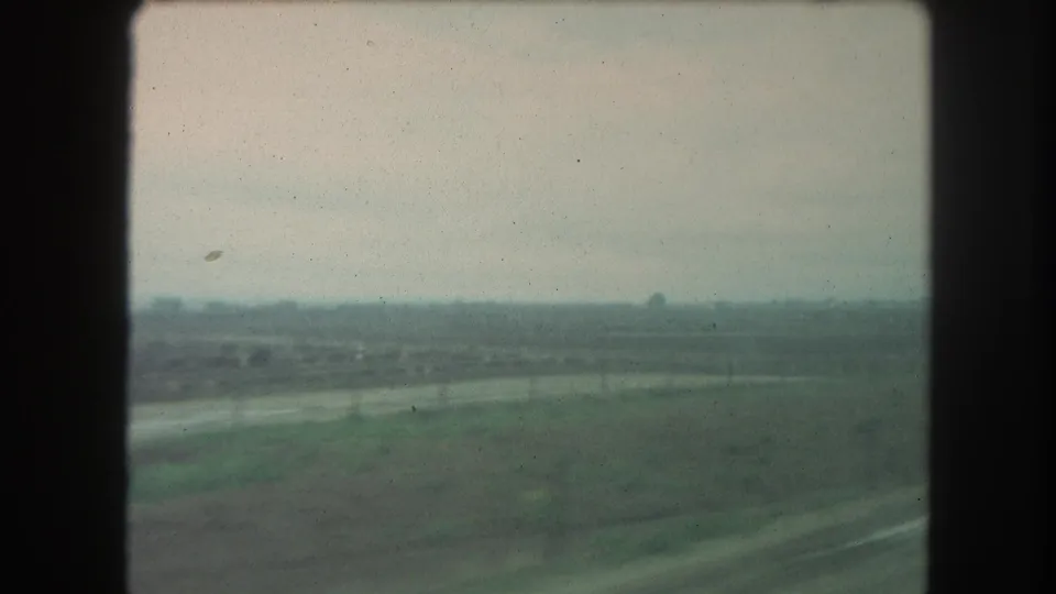 1962 8mm home-movie frame of flat farmland and a distant tree line, viewed from a moving vehicle in the stated Winter Park, Colorado area.