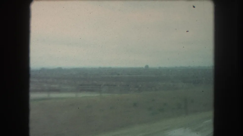 Wide rural landscape from a moving vehicle, with muted fields and soft horizon in 1962 8mm home-movie footage identified as Winter Park, Colorado.