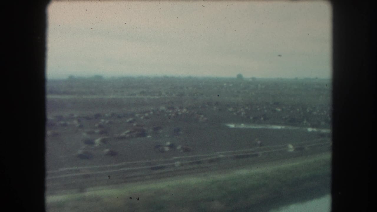 1962 Winter Park, Colorado view from a train window showing open terrain, distant structures, and a hazy horizon on 8mm film.