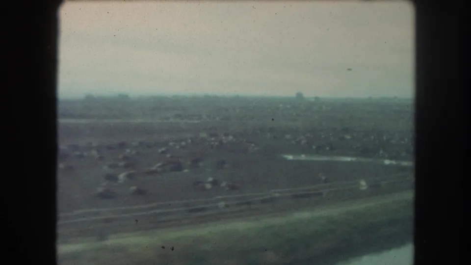1962 Winter Park, Colorado view from a train window showing open terrain, distant structures, and a hazy horizon on 8mm film.