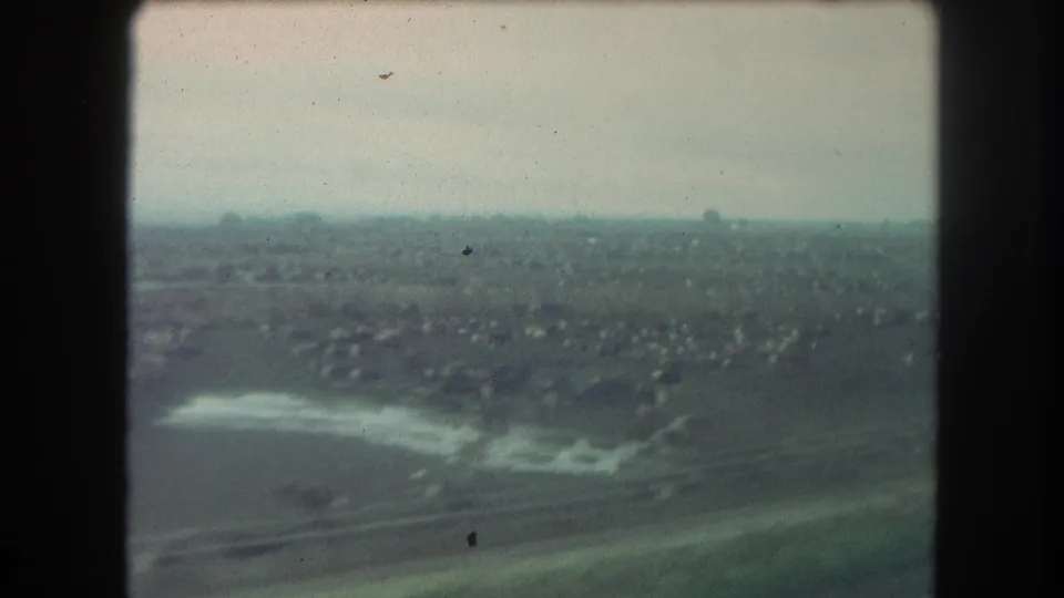 1962 Winter Park, Colorado train-window frame with open land, a reflective water area, transport lines, and small buildings in the distance.