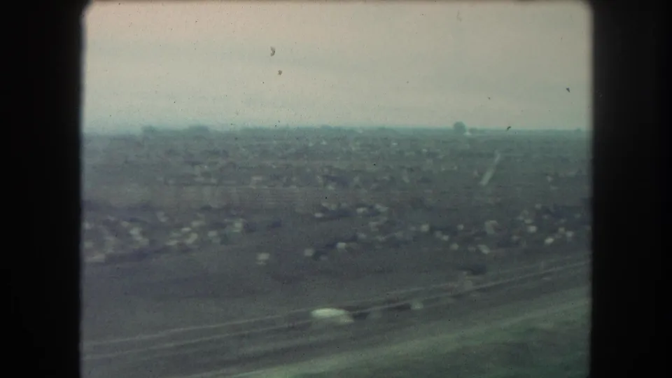 1962 Winter Park, Colorado home-movie frame showing a moving train's view of sparse settlement, open land, and soft distant hills or horizon.