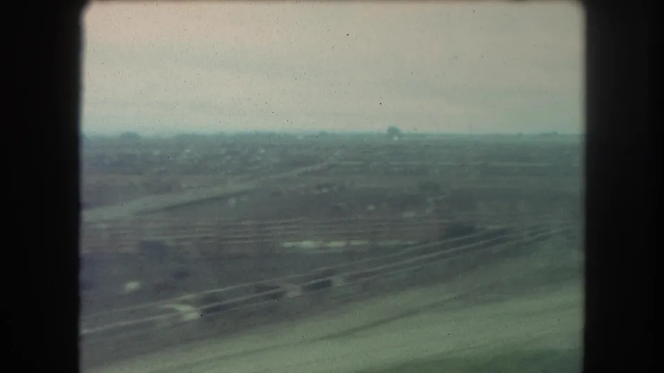 1962 Winter Park, Colorado view through a train window, showing curved transport lines, open fields, distant buildings, and muted 8mm color.