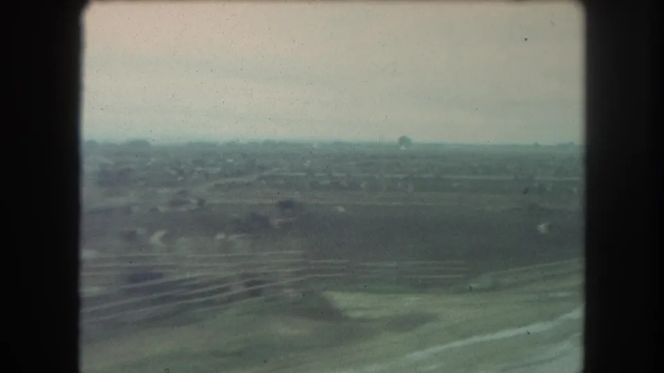 1962 8mm train-window view near Winter Park, Colorado, looking across muted rural fields and a hazy horizon.