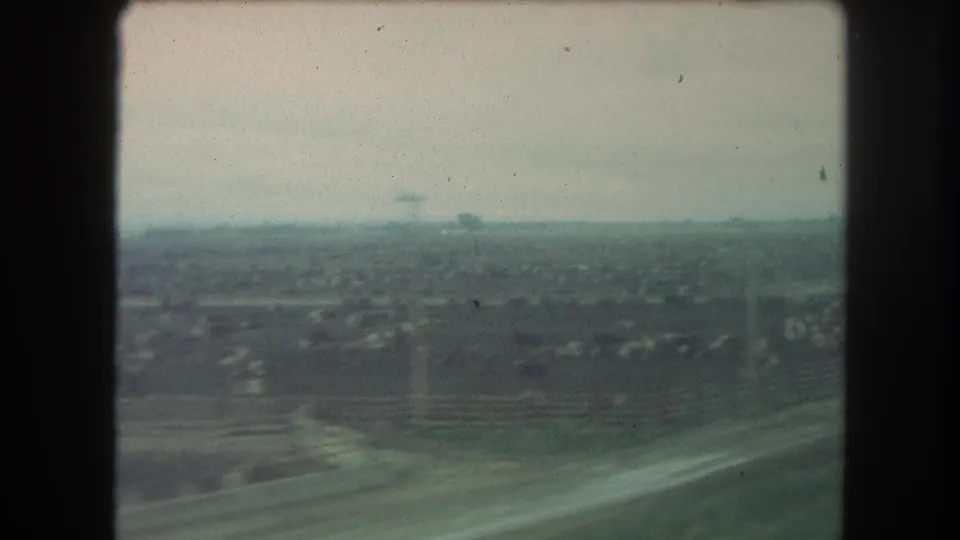 From the moving train, the 1962 8mm frame shows rural fields, small buildings, and a hazy Colorado horizon.