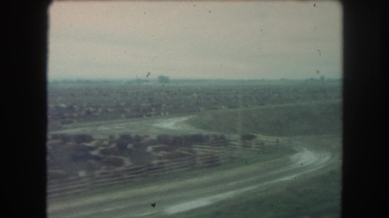 Distant countryside with a curving road, open fields, and low hills under a pale sky.