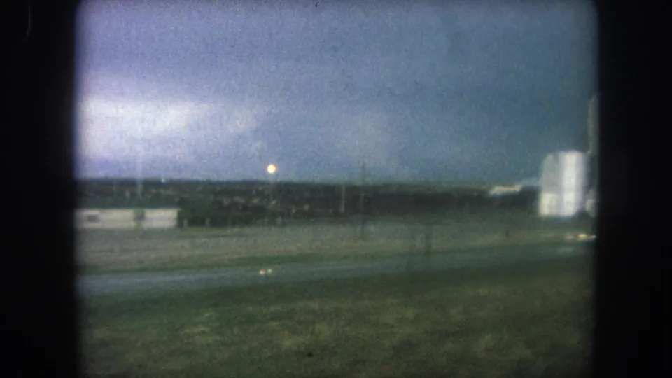 Dusk 8mm frame near Winter Park, Colorado, showing a roadside field, distant buildings, and a pale vertical structure.
