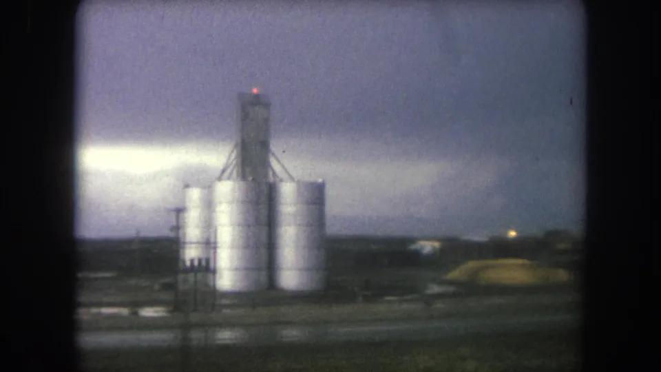 Final 8mm frame from Winter Park, Colorado, showing the silo complex, wet roadside surface, and dark storm clouds.
