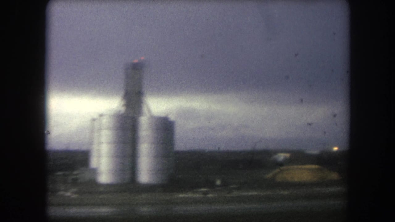 Industrial silos and dark vehicle framing under an overcast sky.