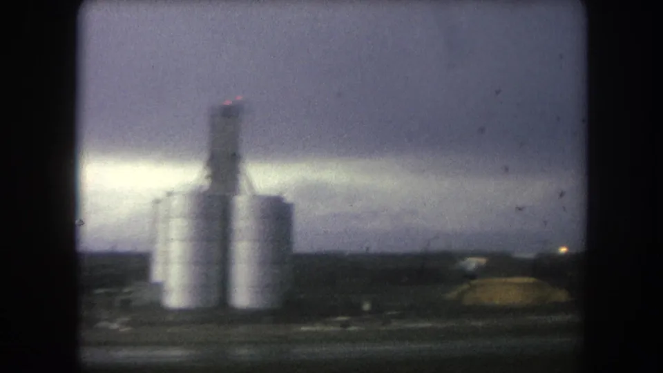 1962 8mm frame from Colorado showing industrial silos beyond a dark vehicle or bridge frame in hazy light.