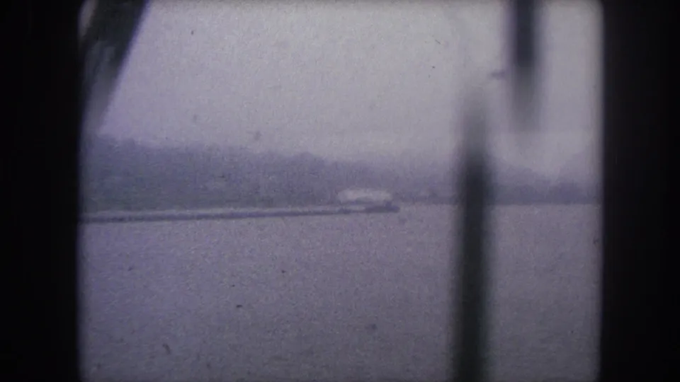 Hazy 1962 8mm travel view over water, with vertical structure obscuring the distant shoreline.