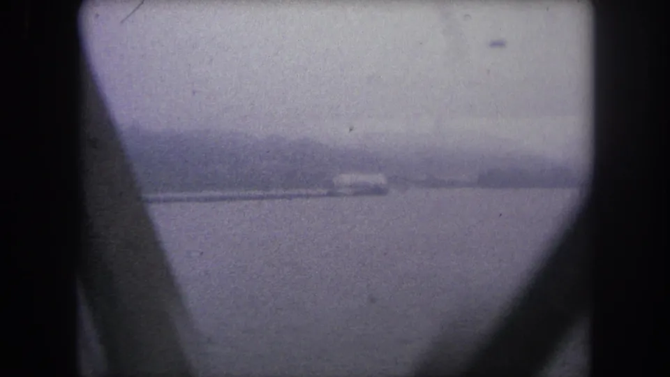 1962 8mm frame of a hazy water view in Colorado, partially obscured by bridge or vehicle structure.