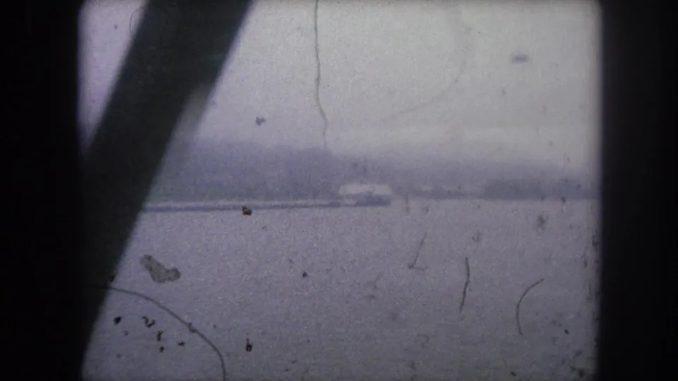 1962 8mm travel view in Colorado showing a wide river or lake, faint shoreline, and dark foreground beams.