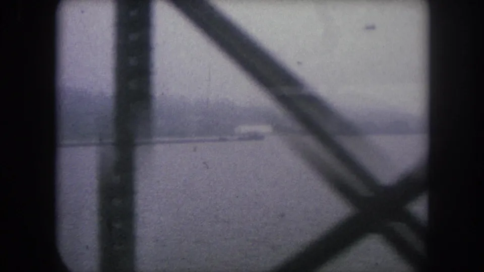 A blurred 1962 Colorado home-movie frame shows water, a faint building on the far side, and heavy foreground beams.