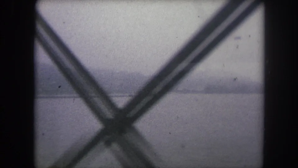 Final 1962 8mm frame with a misty shoreline across water, seen through an X-shaped foreground structure.