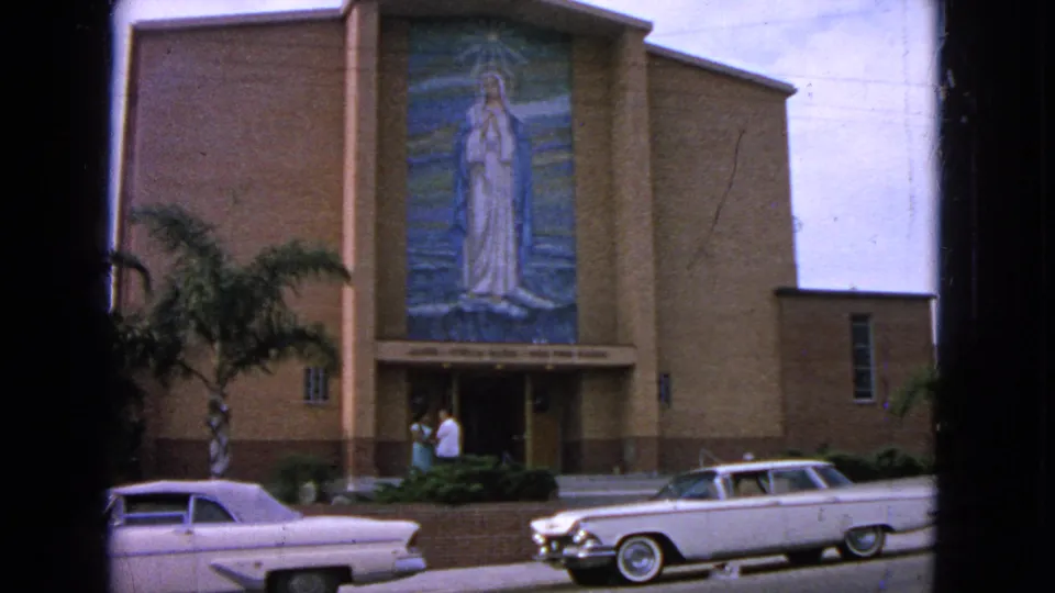 1963 Barrington, Illinois church exterior with a Virgin Mary mosaic above the doors, two white cars parked in front, and adults near the entrance.