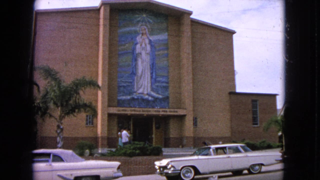 Brick church facade with a large Virgin Mary mosaic above the entrance and cars in front.