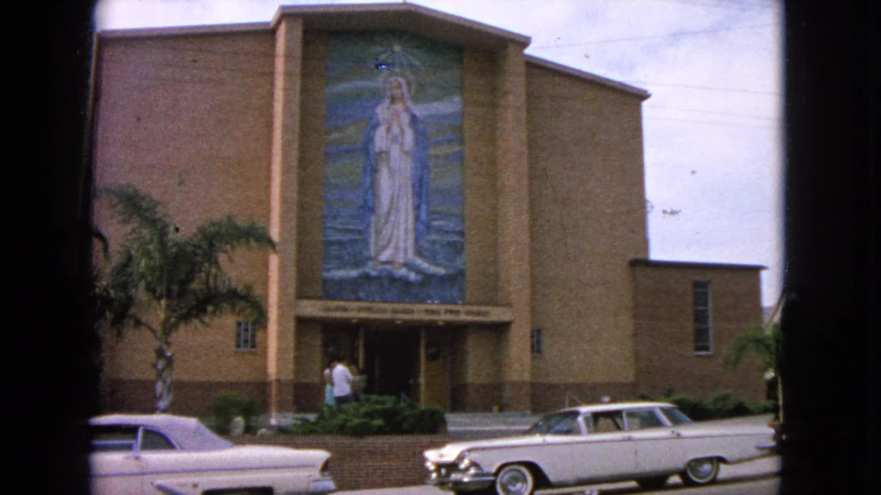 Barrington church facade in 1963 with a tall Virgin Mary mosaic above the entrance and a white mid-century car crossing the foreground.