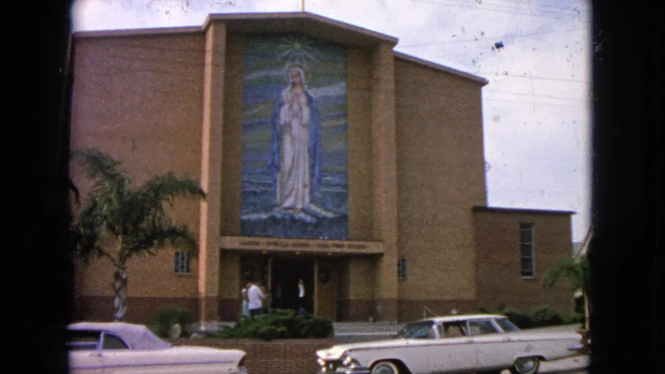 Barrington, Illinois church exterior from 1963 with a large Virgin Mary mosaic, people at the entrance, palm landscaping, and a white 1960s car.