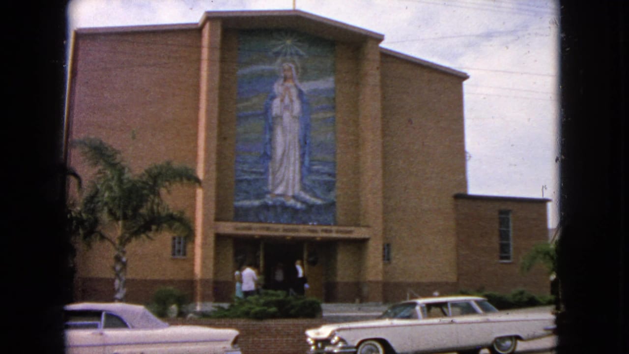Brick church exterior with Virgin Mary mural, parishioners near the entrance, and parked 1960s cars.
