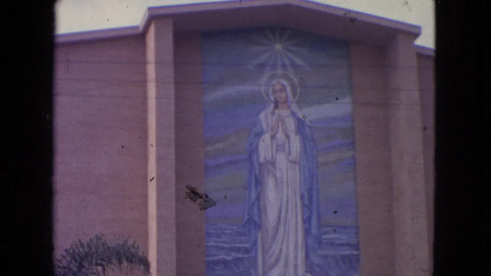 1963 8mm frame from Barrington, Illinois showing the Virgin Mary mural closer in frame on a church exterior.