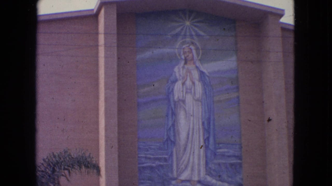1963 Barrington, Illinois home-movie frame of a large Virgin Mary mural on a church exterior, bordered by dark film gate edges.
