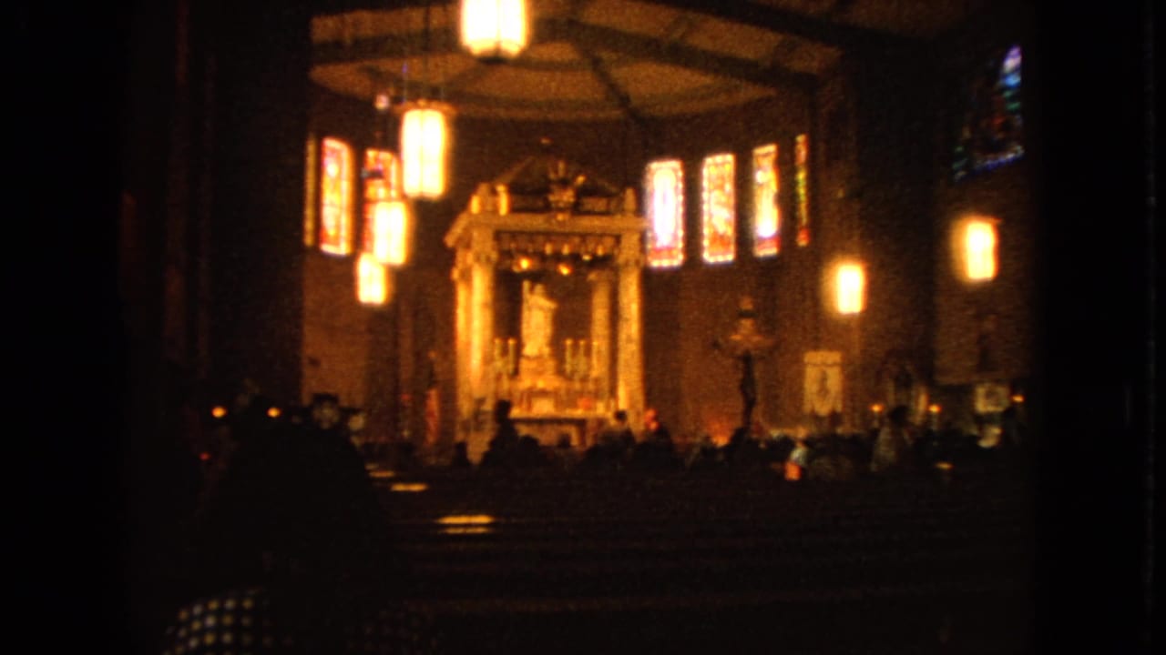 Dim Catholic church nave with pews, hanging lights, stained glass, and distant altar.