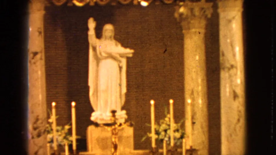 Close 1963 Barrington church view of a white Madonna and baby Jesus statue framed by marble columns, lit candles, and floral arrangements.