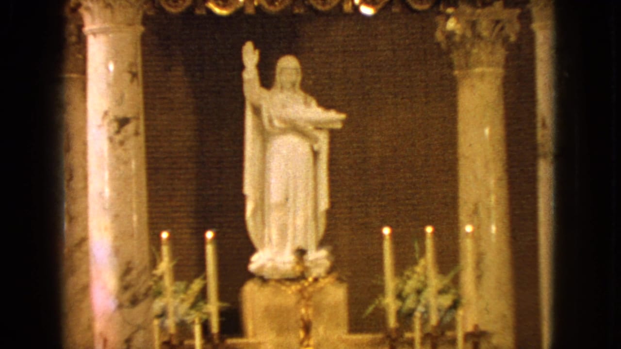 White saint statue on a candlelit altar between marble columns.